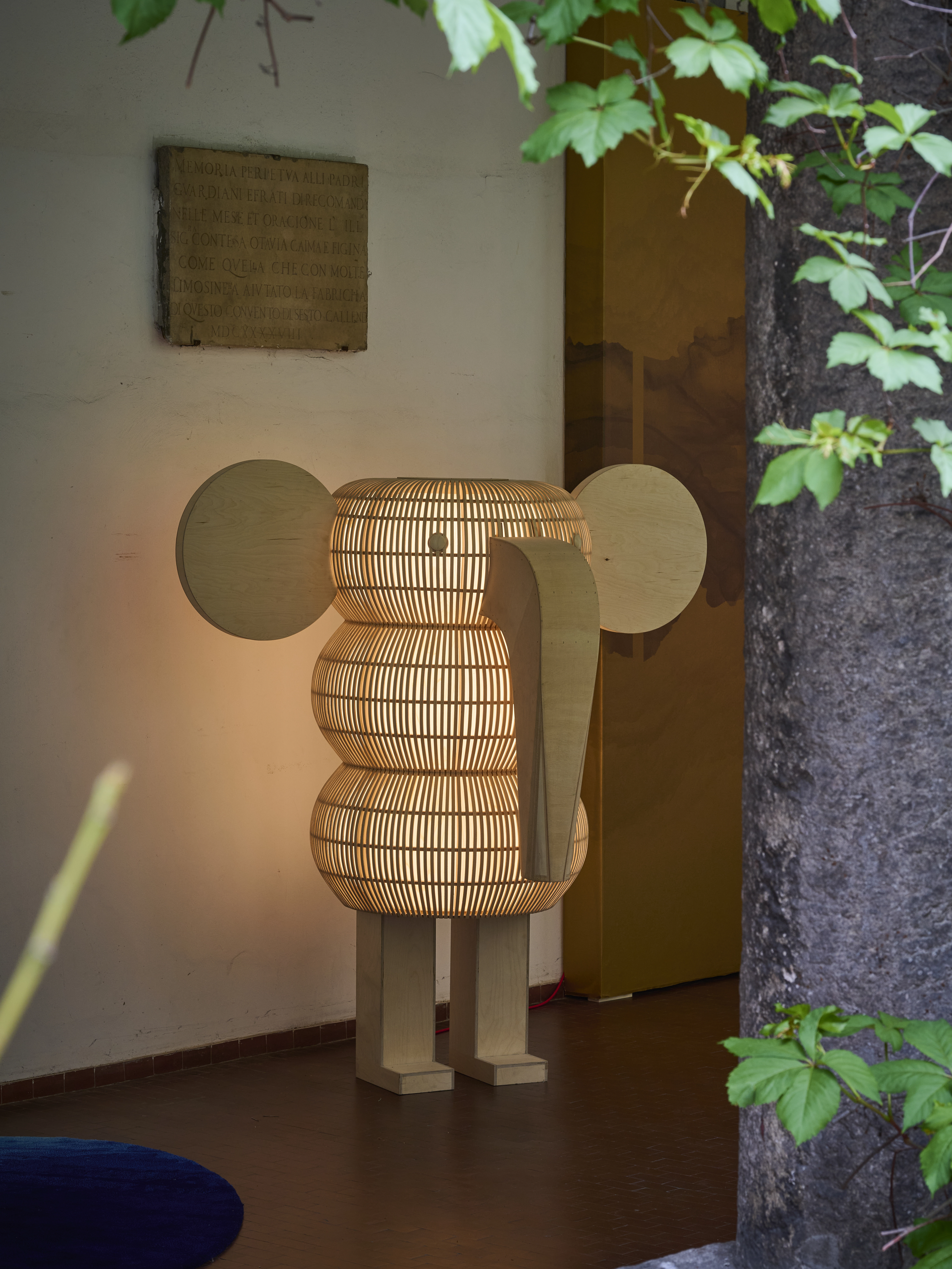 The main character of the image is the floor lamp "Smelly Fant" designed by Isidro Ferrer and Mariví Calvo. It is a luminous sculpture of 1,63 high with the shape of an elephant.