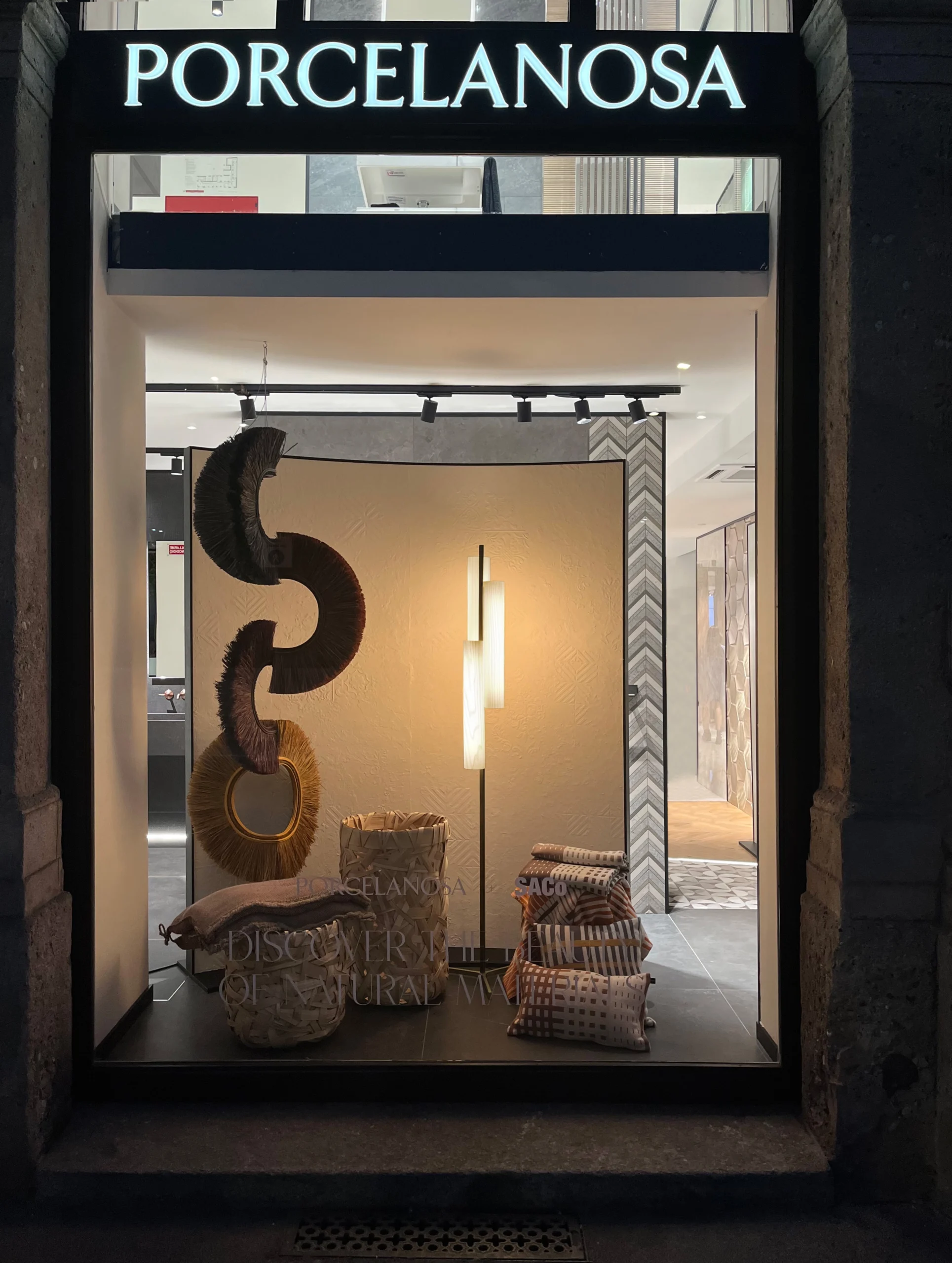 The photo frames a display case in the Porcelanosa shop where you can see the "Blacknote Triplet" floor lamp designed by Ramón Esteve together with other designs by collaborators in the exhibition. 